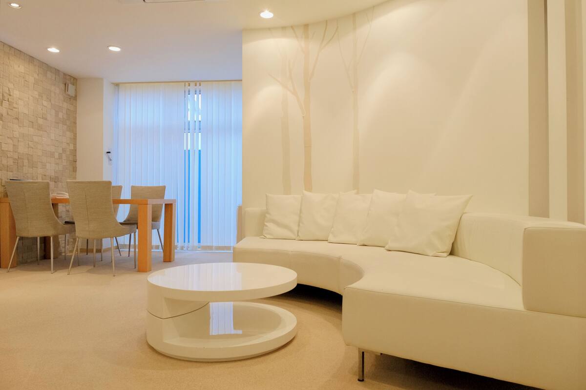 A modern living room with a white sofa, a round coffee table, and a dining area with chairs and a table.