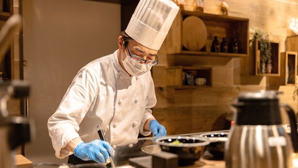 A chef in a white uniform and tall hat, working with kitchen equipment in a well-lit, modern kitchen. - Hotel Naturwald Furano (Furano)
