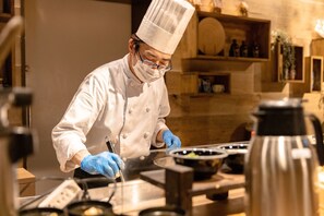 Een kok in een witte uniform en hoge koksmuts, die werkt met keukenapparatuur in een goed verlichte, moderne keuken.