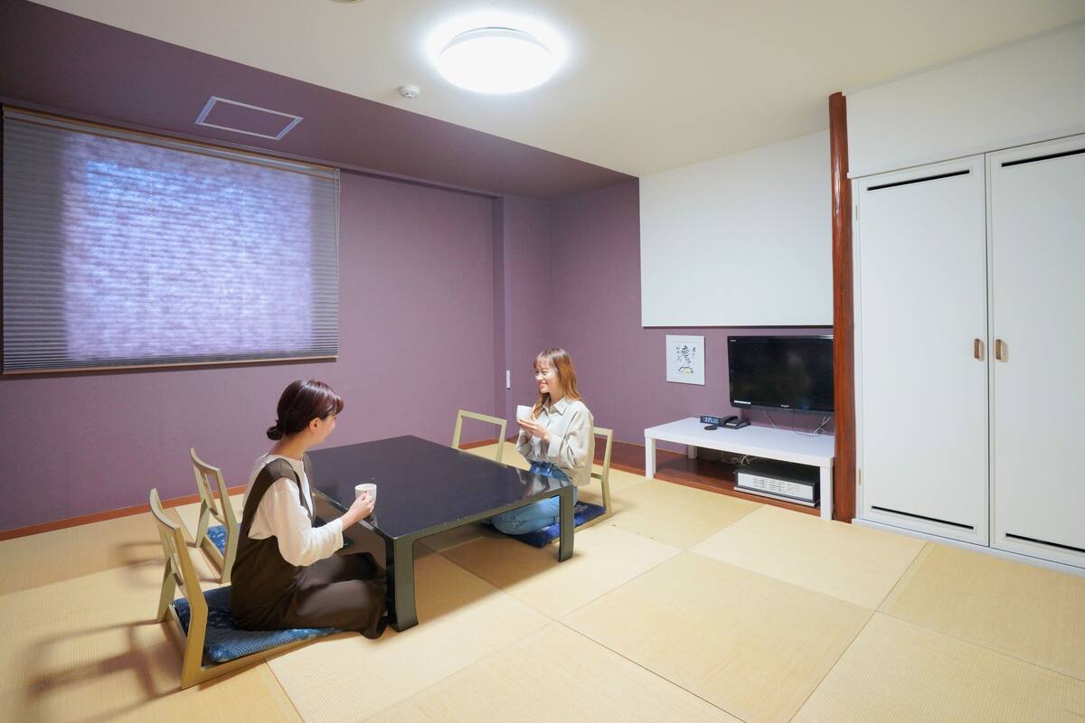 A room with tatami mats, a black table, chairs, a television, and a cabinet.