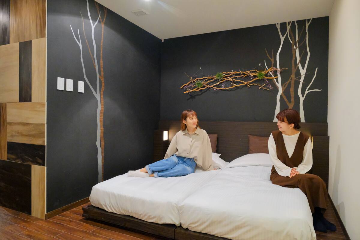A modern bedroom with a large bed, dark walls, and a decorative branch piece.