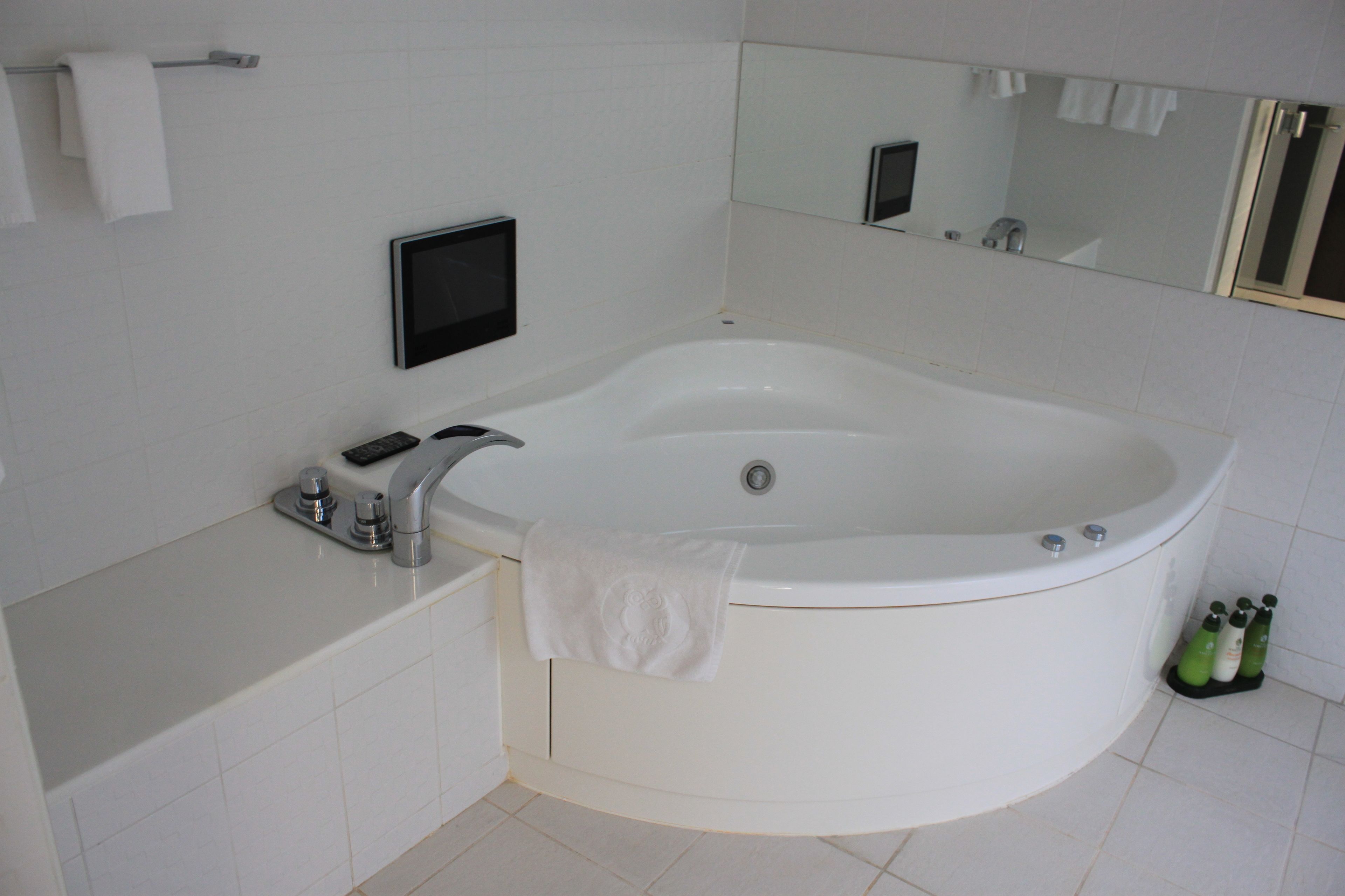 A modern bathroom with a large bathtub, a vanity with a mirror, and a digital screen.