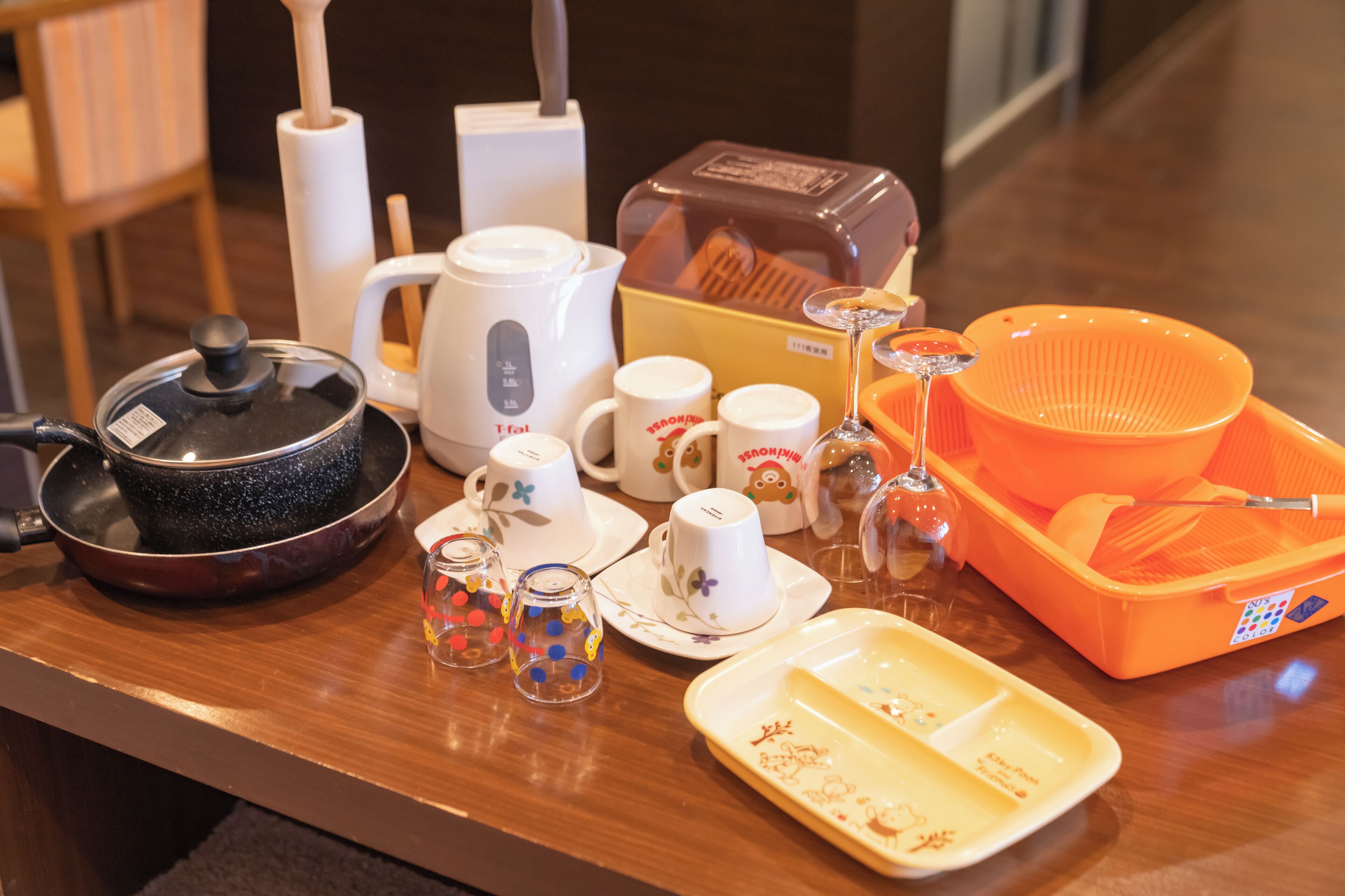 Une table avec une poêle noire, une théière blanche, des tasses blanches, un verre et un plateau jaune contenant des restes de nourriture.
