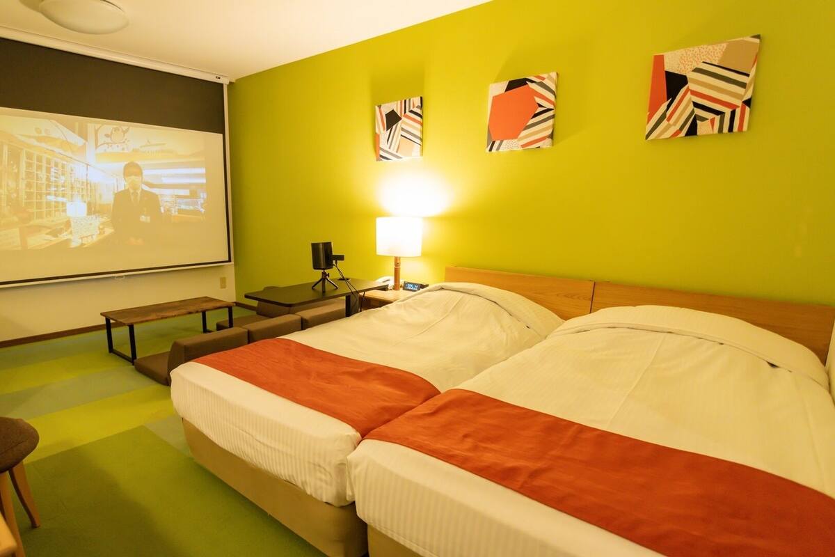 A hotel room with a bed, a desk, a projector screen, and a lamp.