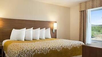 Quarto de hotel com cama, cabeceira, janela com cortinas e luminária na parede.