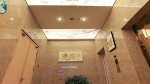 A hotel lobby with a high ceiling, marble flooring, a skylight, recessed lighting, a framed artwork, a fire alarm sign, and a potted plant. - GreenTree Inn Taizhou Gaogang District Gov. Business Hotel (Taizhou)