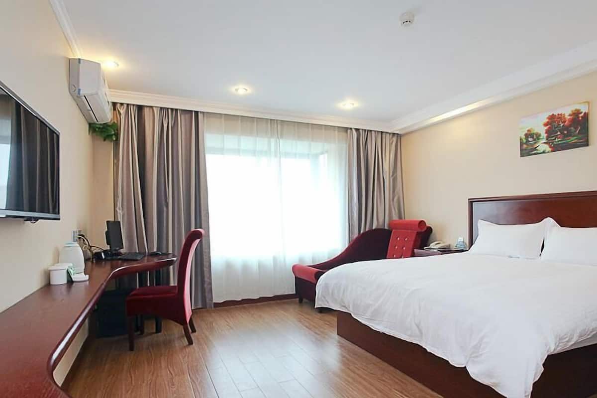 Ett hotellrum med en stor säng, ett skrivbord med en stol, en platt-TV och ett fönster med gardiner.