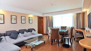 A modern living room with a grey sectional sofa, a glass coffee table, a dining area with a wooden table and chairs, and a large window with curtains. - GreenTree Inn Taizhou Gaogang District Gov. Business Hotel (Taizhou)