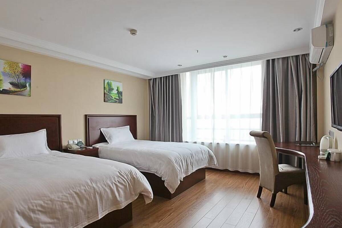 Ett hotellrum med två sängar, ett skrivbord, en stol, en TV och stora fönster med gardiner.