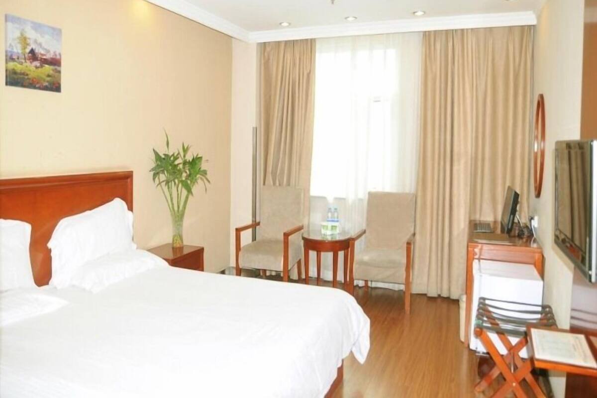 A hotel room with a bed, a desk with a chair, a small table with a chair, and a TV.