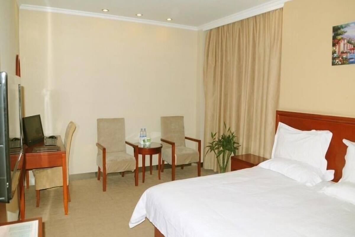A hotel room with a bed, two chairs, a small table with water bottles, a desk with a laptop, and a television.