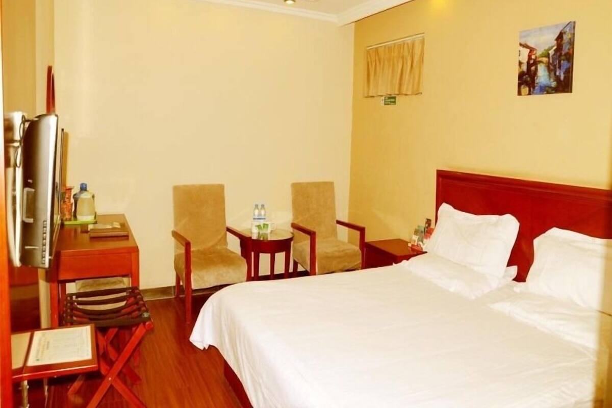 A hotel room with a bed, two armchairs, a small table with a bottle of water, a television, and a painting on the wall.