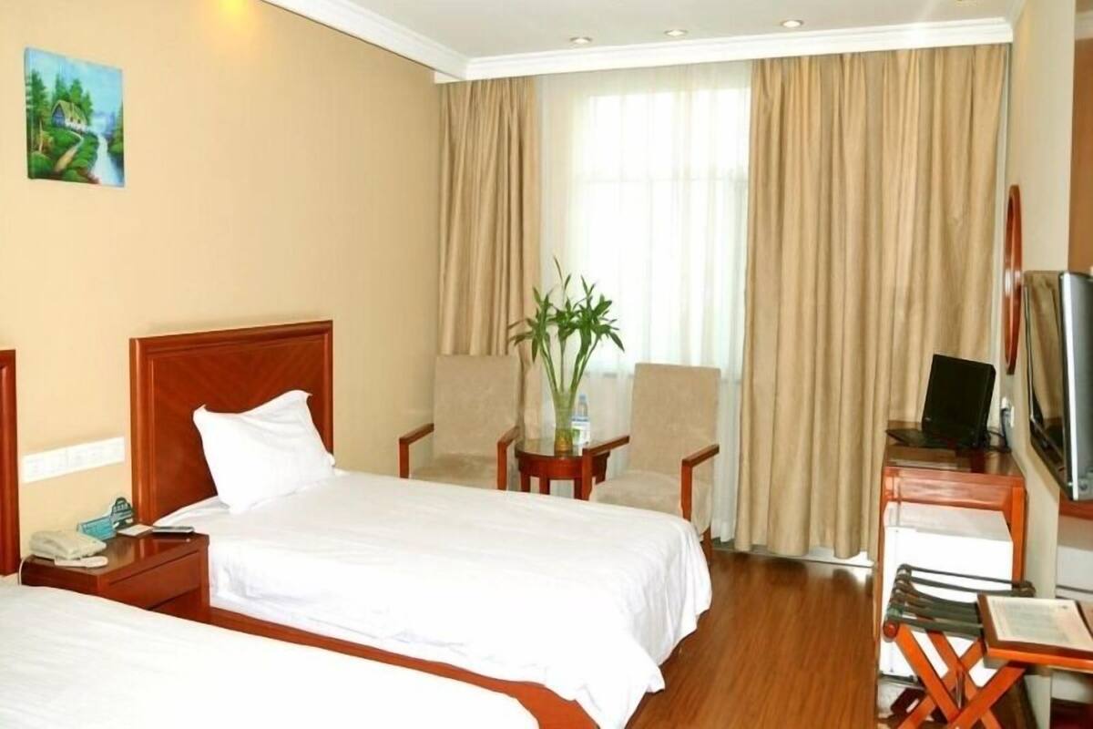 A hotel room with two beds, a desk, a chair, a TV, and a window with curtains.