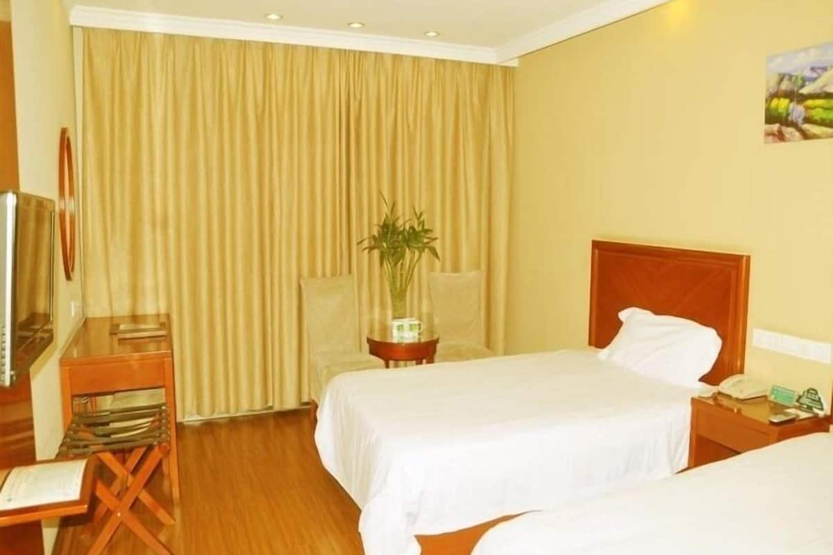 A hotel room with two beds, a desk with a chair, a television, and a large window with curtains.