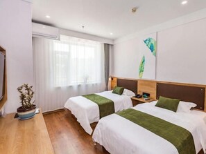 Une chambre d’hôtel avec deux lits, un bureau en bois, une plante en pot et une fenêtre avec des rideaux.