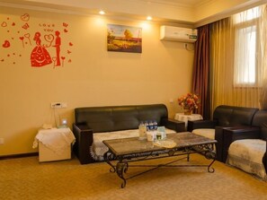 A cozy living room with a black leather sofa, a coffee table with water bottles, a painting on the wall, and a 'Love You' decoration.
