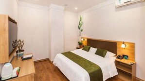 Una habitación de hotel con cama, mesita de noche, lámpara y aire acondicionado.