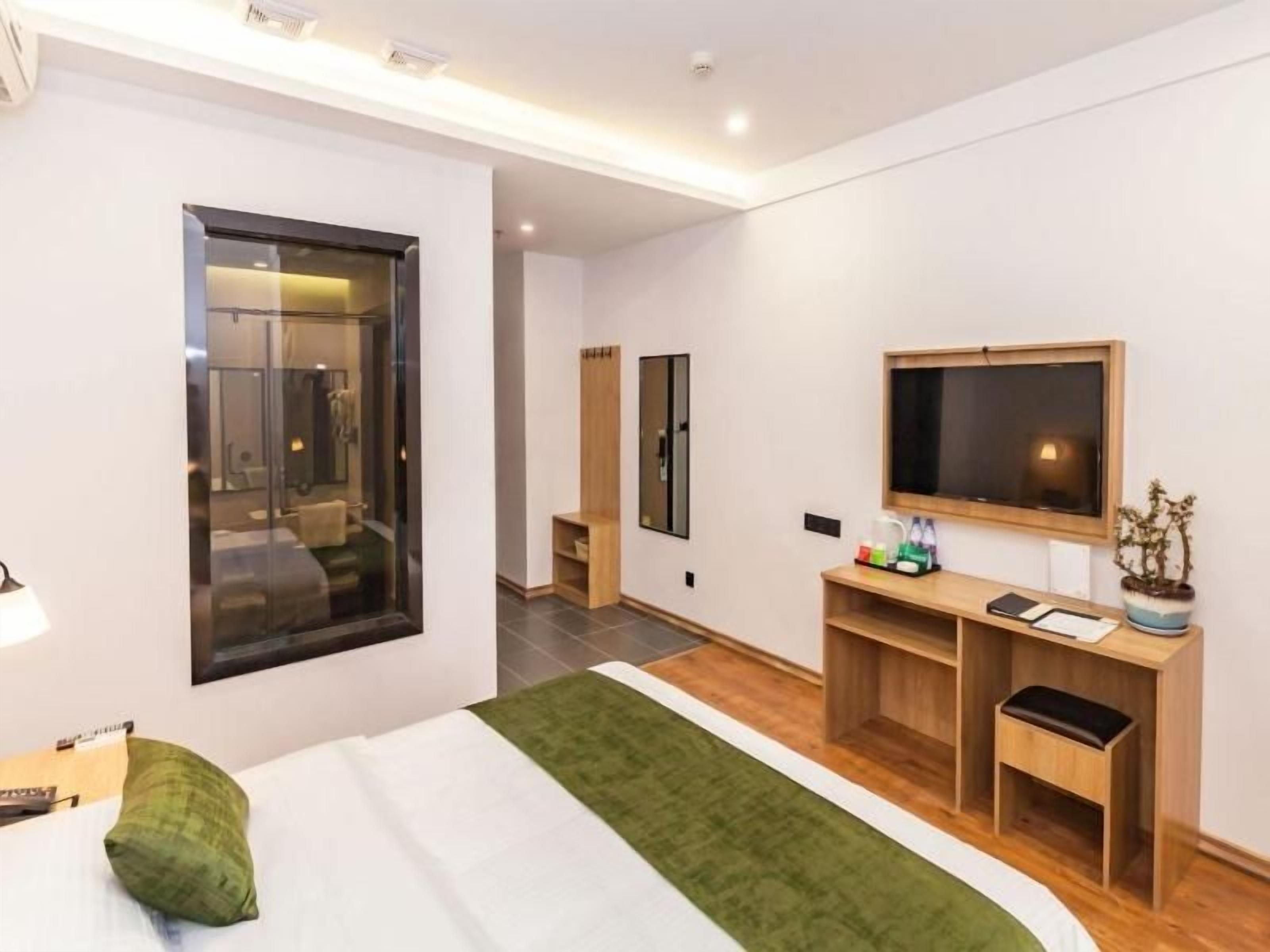 A hotel room with a bed, a TV, a desk, a mirror, and a window.