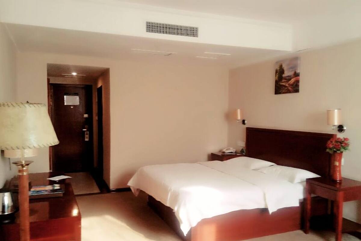 Habitació d'hotel amb llit, taules de nit, una làmpada, una meseta de nit, una porta i un quadre penjat a la paret.