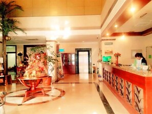 Eine Hotelhalle mit einer Rezeption, einer großen Zimmerpflanze und einem Marmorboden.