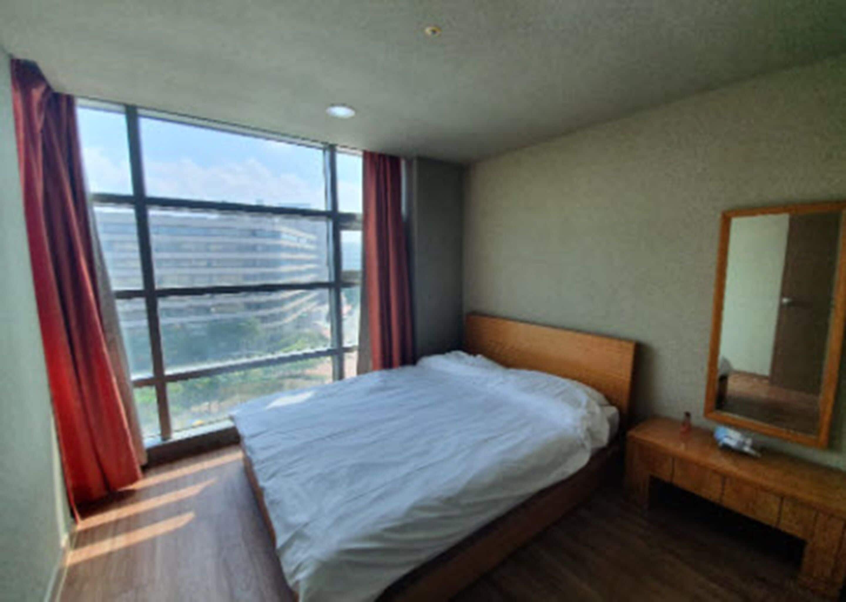 Ein Schlafzimmer mit großem Fenster, einem Bett, einem Nachttisch und einem Spiegel.