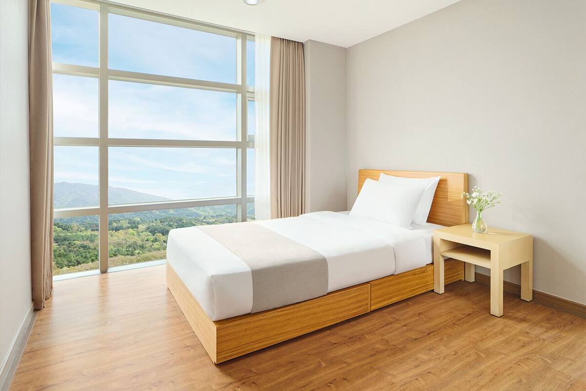 Habitación de hotel moderna con un ventanal grande, una cama de madera, una mesita de noche y vistas al exterior.