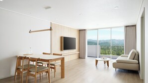 Un salon moderne comprenant un coin repas, un téléviseur à écran plat fixé au mur, un balcon avec vue sur les montagnes et un canapé.