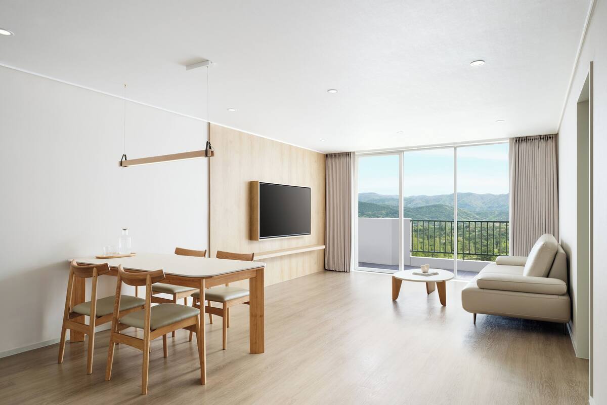 Una sala moderna con comedor, televisor de pantalla plana en la pared, balcón con vistas a las montañas y un sofá.