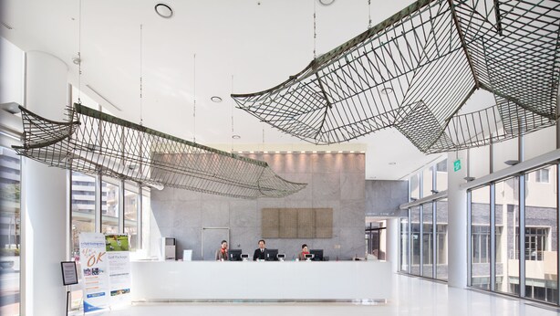 Un hall d’entrée spacieux avec un comptoir de réception, de grandes fenêtres et des structures suspendues en forme de réseau.