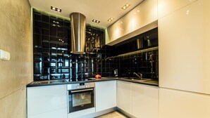 A modern kitchen with a stainless steel range hood, black backsplash, and a built-in oven. - Oxygen Central Apartments (Warsaw)