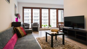 A living room with a sofa, armchairs, a coffee table, a TV, and large windows with a view of buildings. - Oxygen Central Apartments (Warsaw)