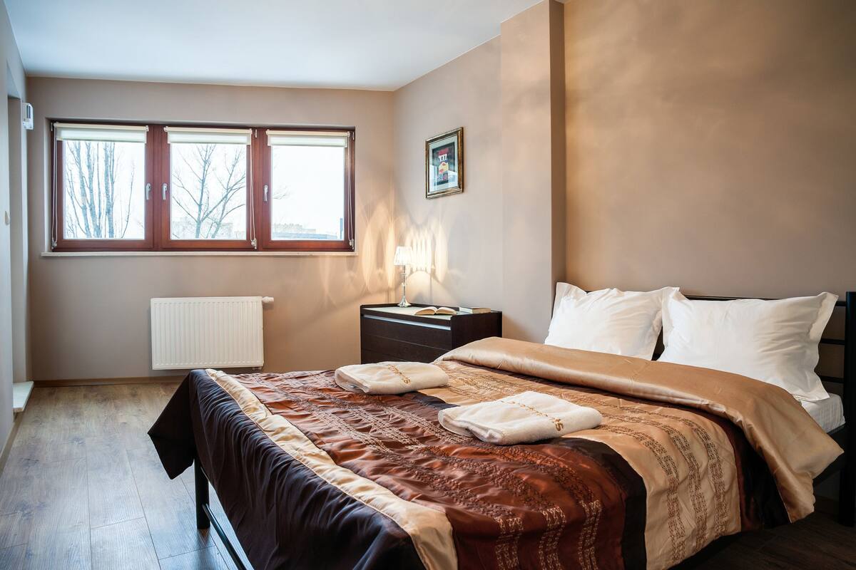 A bedroom with a bed, a nightstand, a window, and a radiator.