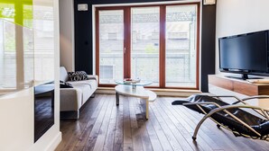 A modern living room with a sofa, a glass coffee table, a TV, and a large window with blinds. - Oxygen Central Apartments (Warsaw)