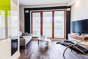 Una sala de estar moderna con un sofá, una mesa de centro de vidrio, un televisor y un ventanal con persianas.