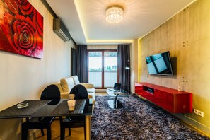 Una sala de estar moderna con un sofá, una mesa de comedor, un televisor montado en la pared y un gran ventanal con vistas.