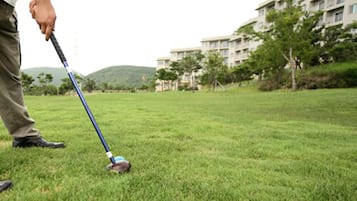 Uma pessoa jogando golfe em um campo de grama bem cuidado, com um edifício ao fundo.