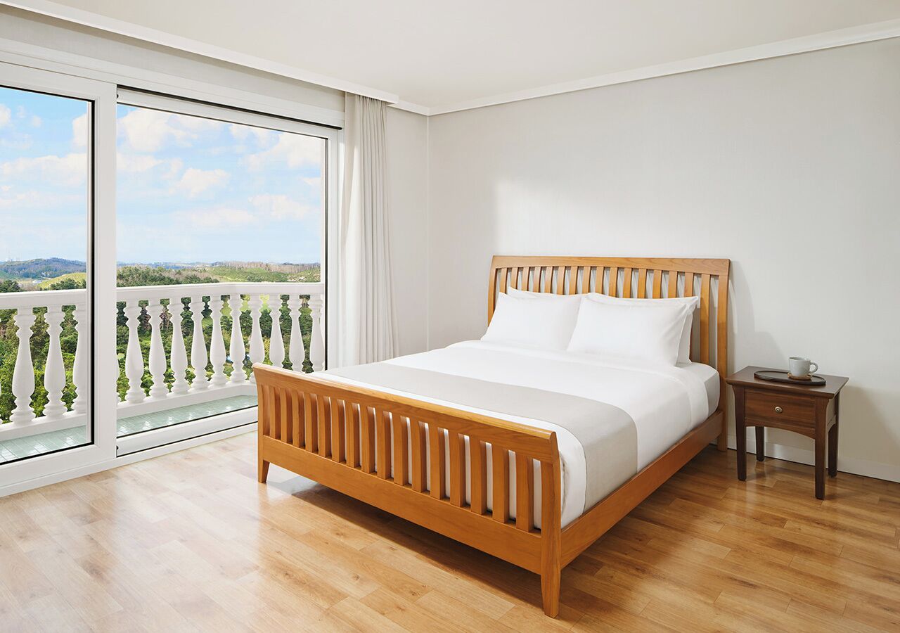 A bedroom with a wooden bed, a nightstand, and a view of a balcony with a railing.