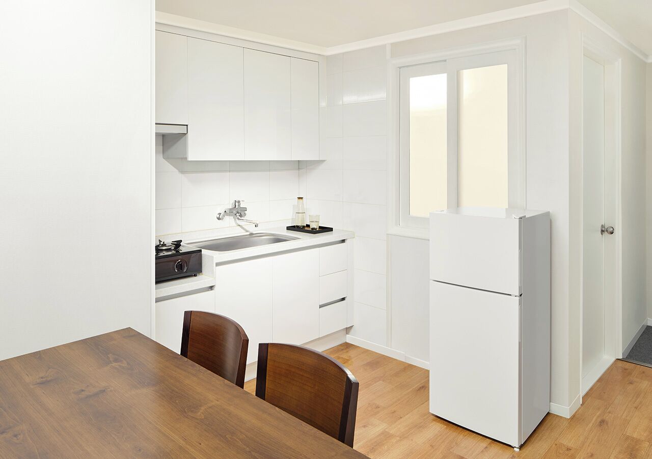 A compact kitchen with white cabinets, a sink, a stove, and a refrigerator. There is a wooden dining table with two chairs.