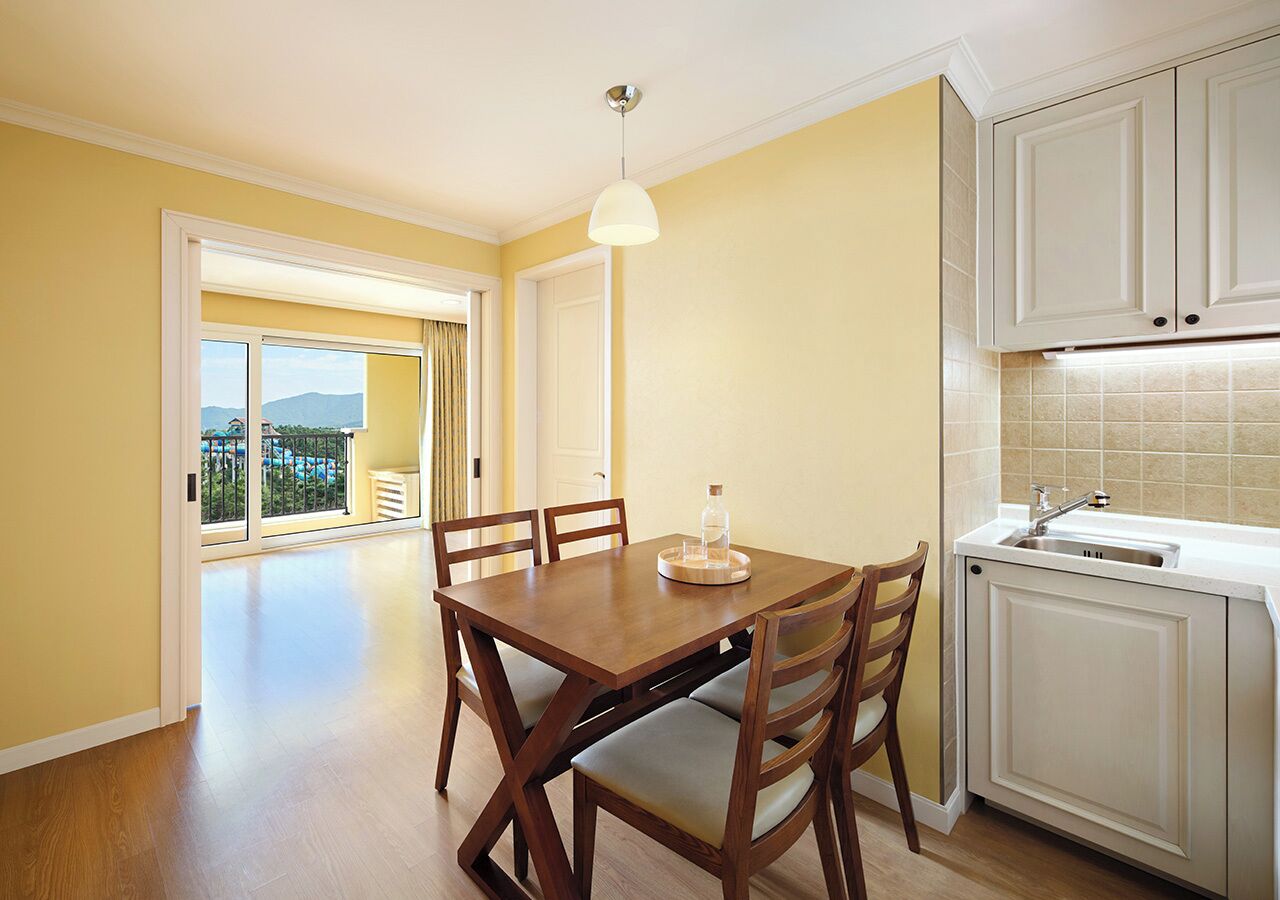 A dining area with a wooden table and chairs, a pendant light, and a view through a glass door to an outdoor balcony.