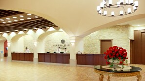 A hotel reception area with a stone wall, wooden reception desks, and a central table with a vase of red flowers. - Hanwha Resort Seorak Sorano (Sokcho)