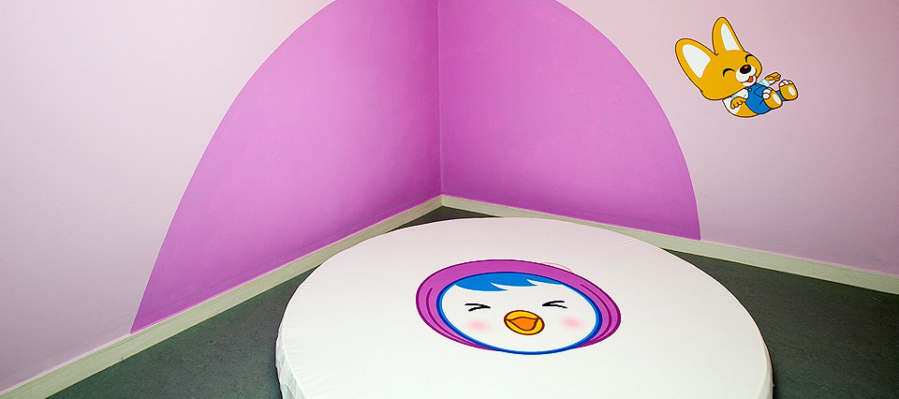 A room with a white toilet, a pink wall, and a cartoon character on the wall.