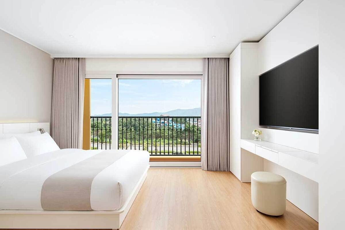 Ein modernes Hotelzimmer mit einem großen Bett, einem Flachbildfernseher, einem Balkon mit Bergblick und Holzboden.