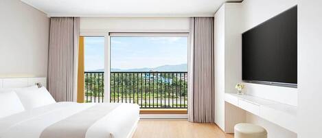 A modern hotel room with a large bed, a flat-screen TV, a balcony with a view of the mountains, and a wooden floor.