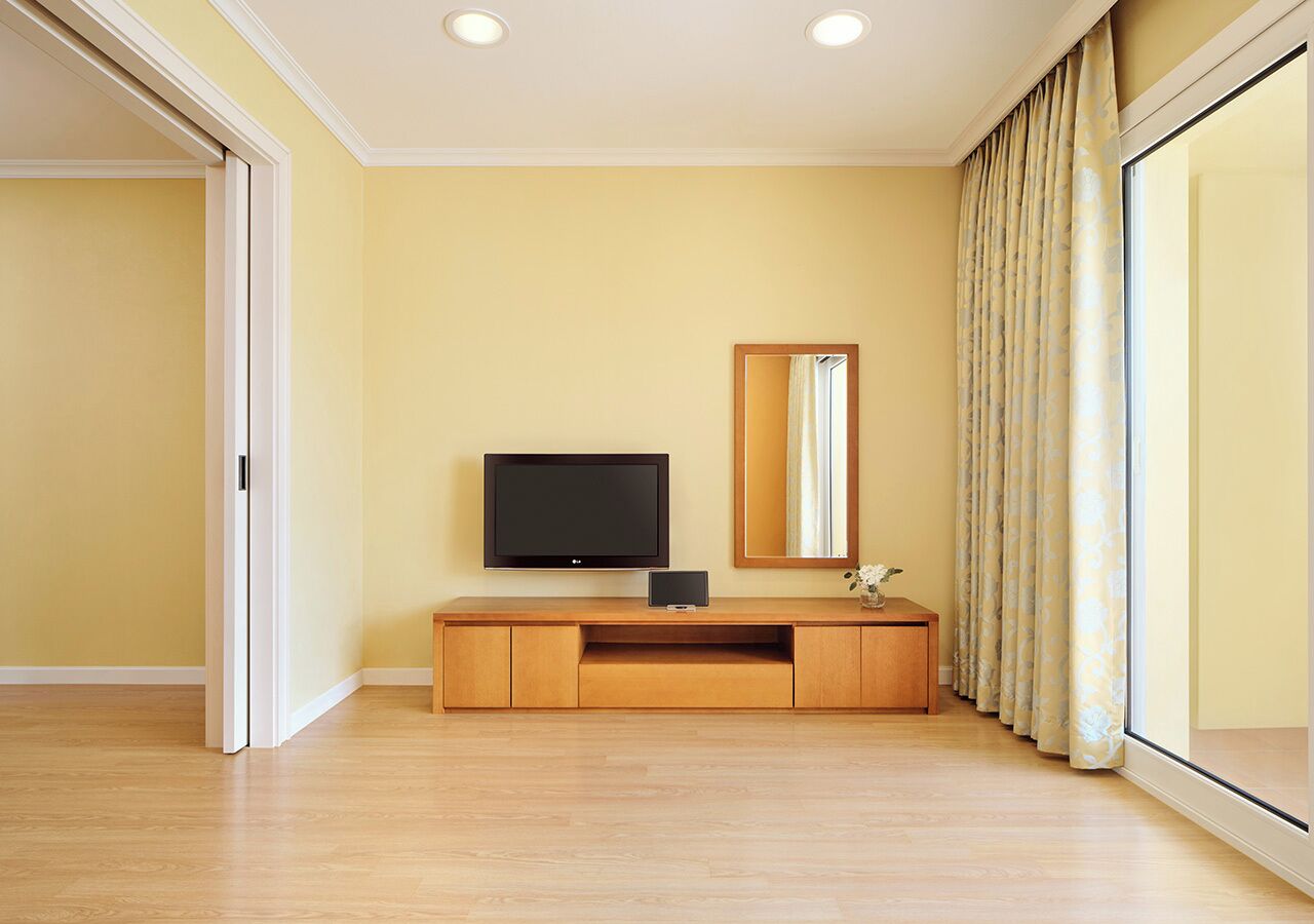 Une pièce comprenant un meuble de rangement en bois pour les appareils multimédias, un téléviseur à écran plat, un miroir et une grande fenêtre avec des rideaux.