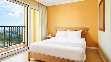 A hotel room with a large bed, a nightstand, a window with a view of a resort, and a balcony.