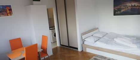 Une chambre avec un lit, un coin repas avec des chaises orange et une vue sur le paysage urbain.