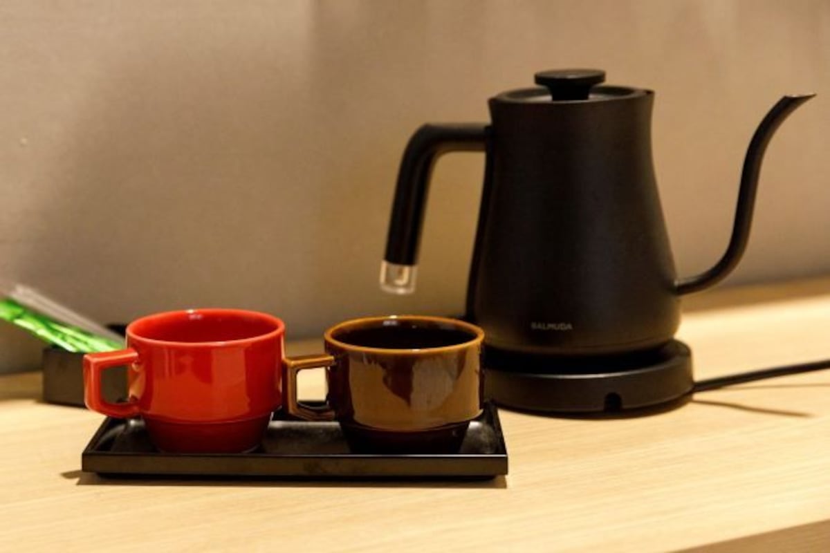 A black electric kettle on a tray with two cups, one red and one brown, on a wooden surface.