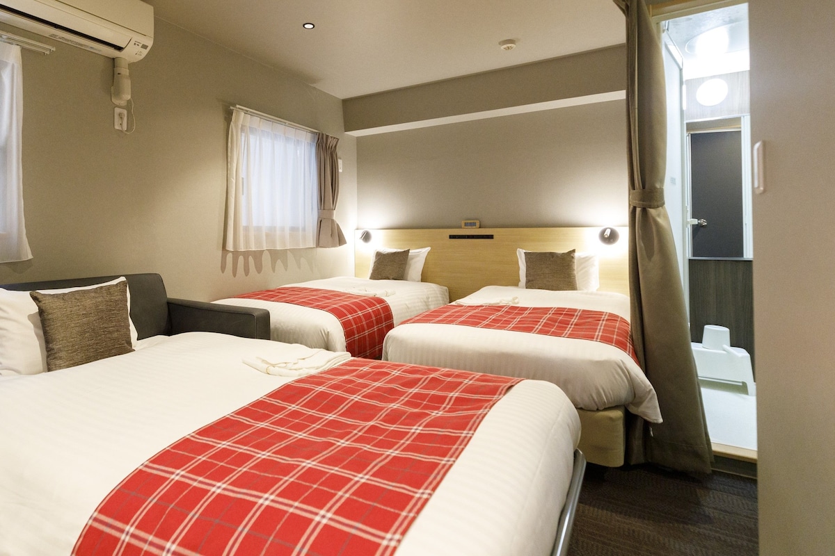 Quarto de hotel com duas camas, um sofá e uma janela com cortinas.