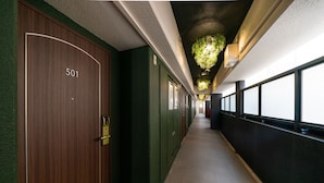 Um corredor com uma porta de madeira identificada como '501', paredes verdes e um teto com plantas pendentes.