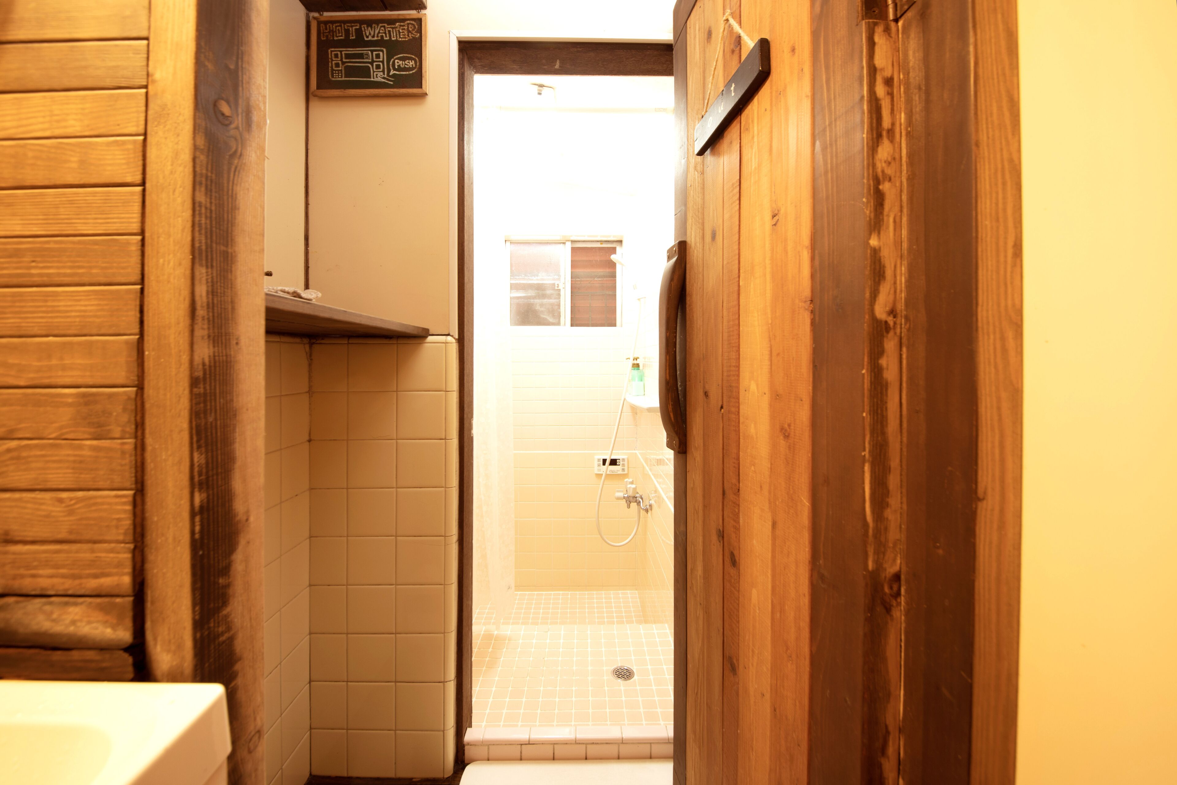 Un couloir étroit aux murs en bois, et une cabine de douche carrelée visible à travers une porte ouverte.